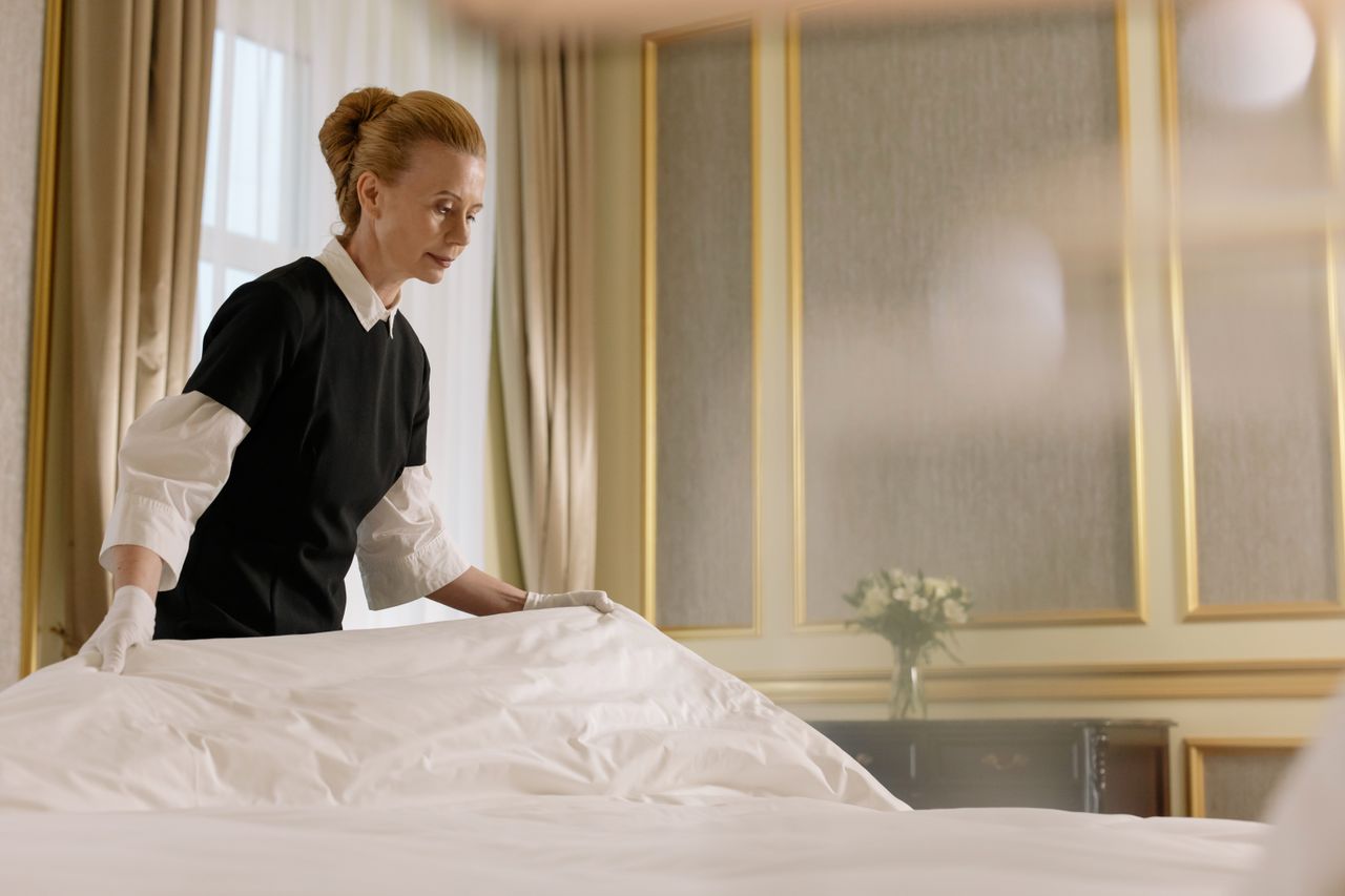 services-03 A professional housekeeper fixes a bed in a luxurious hotel room.