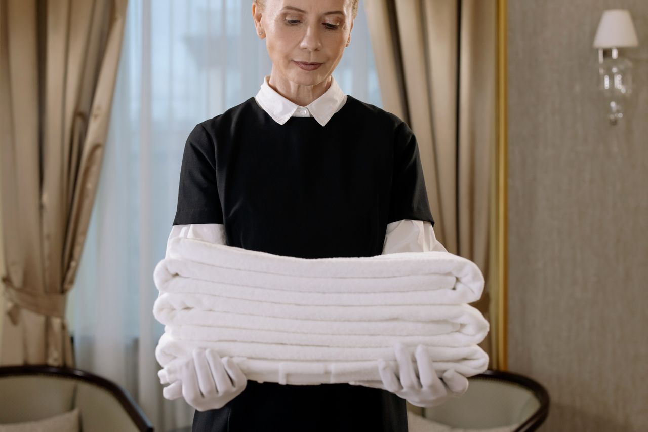 why-choose-us Professional housekeeper holding a stack of fresh towels in a luxurious hotel room, showcasing elegance and service.